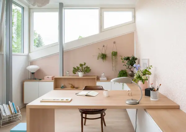 Une petite chambre avec bureau, lumineuse et décorée de plantes. Le bureau en bois clair est prêt pour le travail ou la lecture.